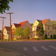 a street corner with houses in the background and trees on both sides, at sunset