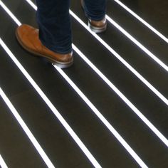 a person wearing brown shoes and jeans standing on a black floor with white lines behind them