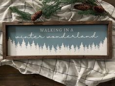 a wooden sign that says walking in a winter wonderland with pine cones and evergreen trees