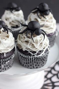 cupcakes decorated with white frosting and black spider decorations on a cake plate