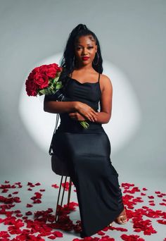 a woman is sitting on a chair with roses around her and holding a bouquet of red roses