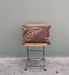 a small wooden bench sitting next to a gray wall with a colorful pillow on it