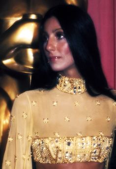 a woman in a yellow outfit standing next to a gold statue and wearing a necklace