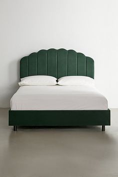 a bed with a green headboard sitting on top of a cement floor next to a white wall