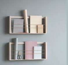 two wooden shelves with books, binders and scissors on them against a gray wall