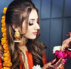 a woman in an orange and red outfit with flowers around her neck holding a flower