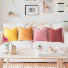 a living room with white couches and colorful pillows on the coffee table in front of it