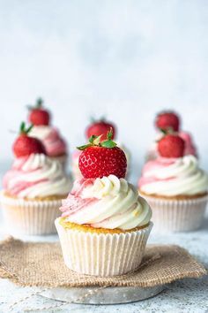 three cupcakes with white frosting and strawberries sitting on top of each other