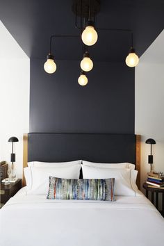 a bed with white sheets, pillows and lamps on the headboard in a bedroom