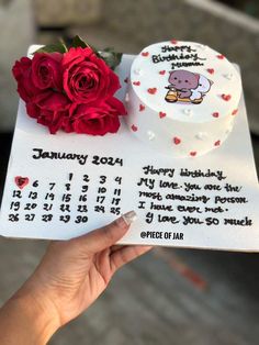 someone holding up a calendar cake with a red rose