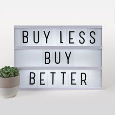 a sign that says buy less, buy better next to a succulent