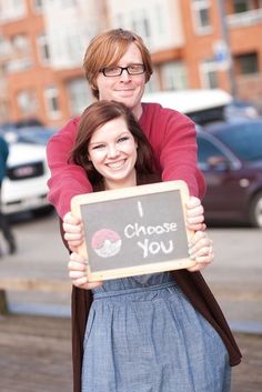 a man and woman hugging each other while holding a chalkboard that says i choose you