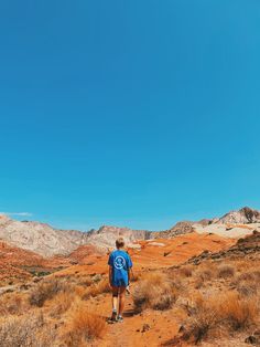 a person with a backpack is walking on a dirt path in the desert under a blue sky