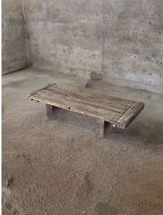 a wooden bench sitting in the middle of a cement room next to a concrete wall