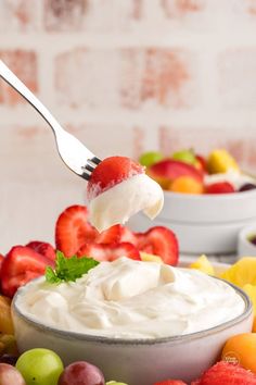 a spoonful of fruit dip with whipped cream on top and fresh fruit in the background