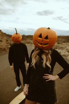 two people wearing pumpkin heads walking down the road with their hands on their hipss