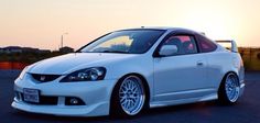 a white car is parked in a parking lot with the sun setting behind it,