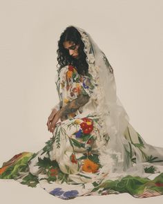 a woman sitting on the ground in a dress with flowers and leaves around her body