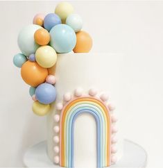 a white cake topped with a rainbow and balloons