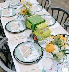 a table set with plates, flowers and a toy truck on it's side