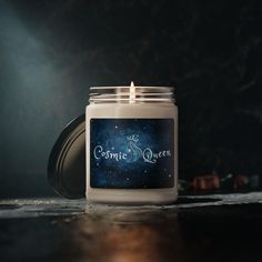 a candle with the words cosmic queen written on it sitting on a table in front of a dark background