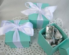 three boxes with silver foil wrapped in white ribbon and bows on top of a doily