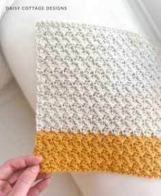 someone is holding up a crocheted pillow with yellow and white squares on it