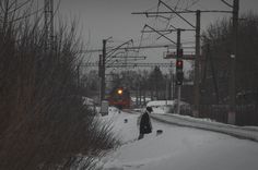 a person walking down a snowy road with a train on the tracks in the background