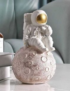 an astronaut figurine sitting on top of a white ball next to a book