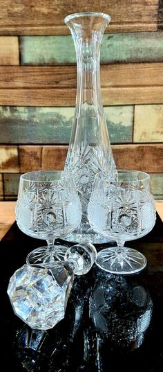 an old fashioned glass decanter and four glasses on a black table with wood planks in the background