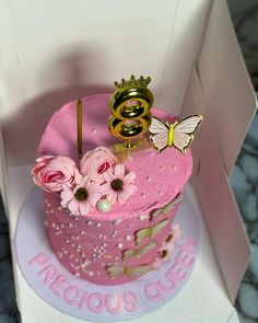 there is a pink cake in the box with flowers and a gold ring on top