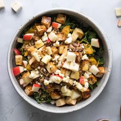 a salad with apples, cheese and other toppings in a bowl on a table