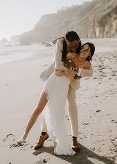 a bride and groom hug on the beach in front of cliffs during their elopement