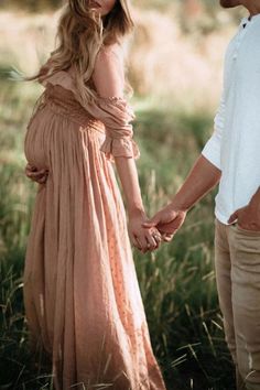 a pregnant woman in a long dress holding hands with a man standing next to her