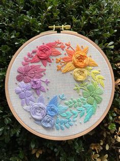 a cross stitch pattern with flowers on it in front of some green plants and bushes