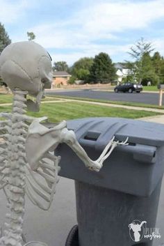 a skeleton sitting on top of a trash can