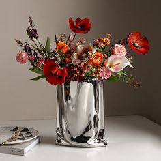 a vase filled with lots of flowers on top of a white table next to a book