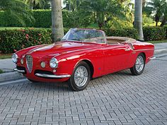 an old red convertible car parked on the side of the road in front of some palm trees