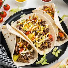 three tacos on a plate with lettuce, tomatoes and other toppings