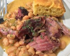 a white plate topped with beans and meat next to a piece of bread on top of a table