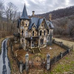 an old abandoned house in the middle of a country road with a fence and gate