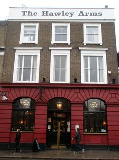 two people walking in front of a red building with white windows and the words the harvey arms on it