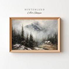 a painting hanging on the wall next to a frame with an image of mountains and trees