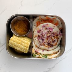 a metal container filled with food next to a corn on the cob and dipping sauce