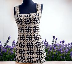 a black and white crocheted dress on a mannequin next to purple flowers