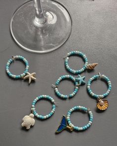 several bracelets with shells and seashells on them next to a wine glass