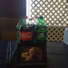 two soda bottles sitting on top of a table next to a framed yoda star wars poster