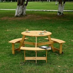 a wooden picnic table with two benches in the grass near some trees and one bench has a book on it