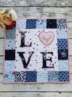 a patchwork quilt with the word love written on it and a flower sitting next to it