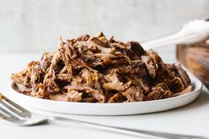 a white plate topped with shredded meat next to a fork